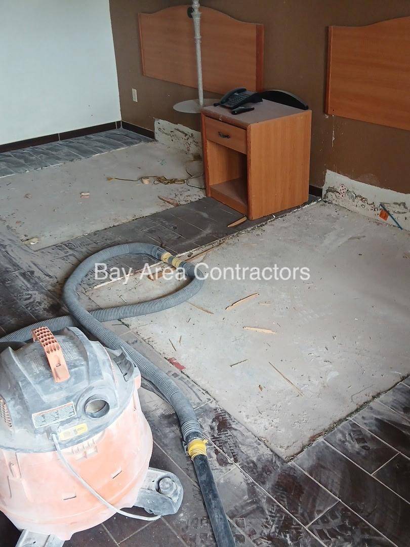Floor tile removed down to the slab during demolition, with a shop vacuum in the foreground