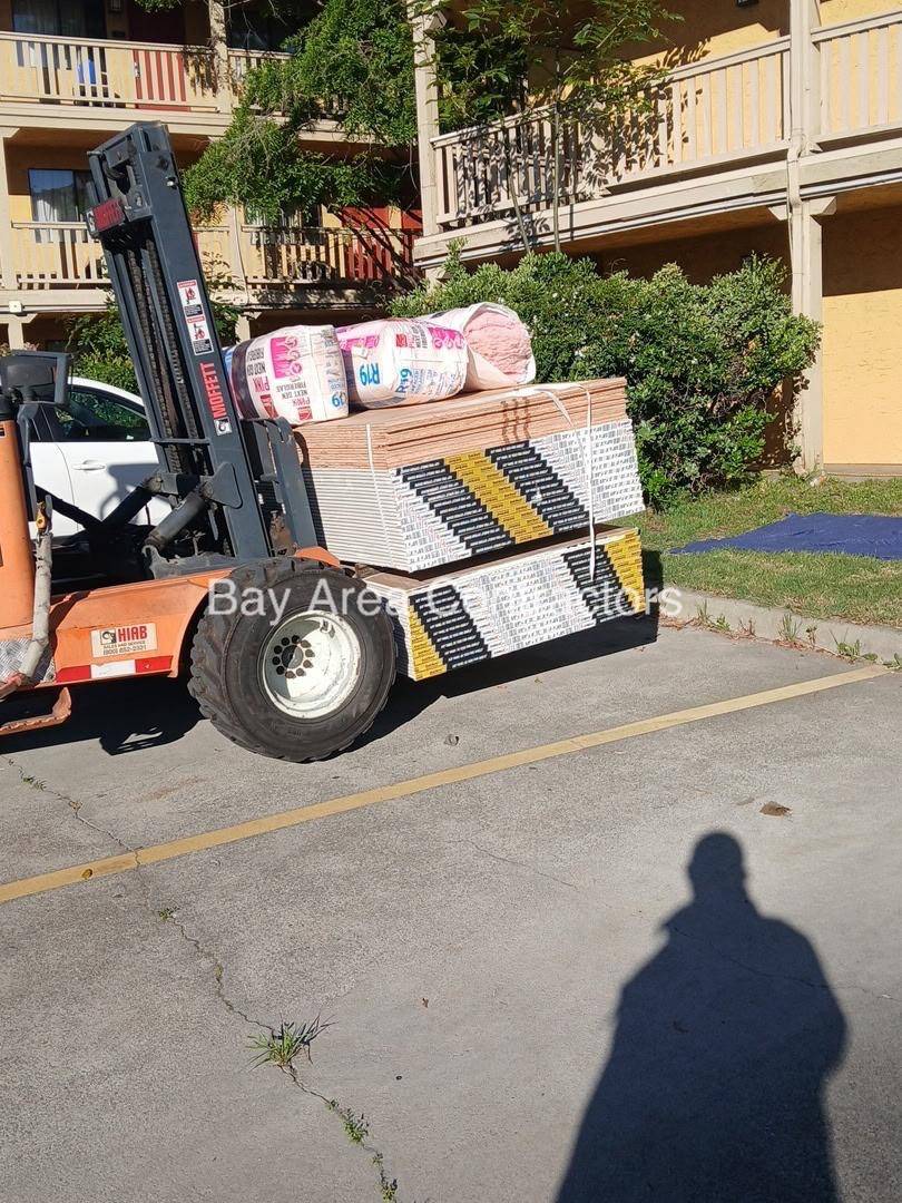Forklift carrying a banded stack of drywall and rolls of insulation across a job site