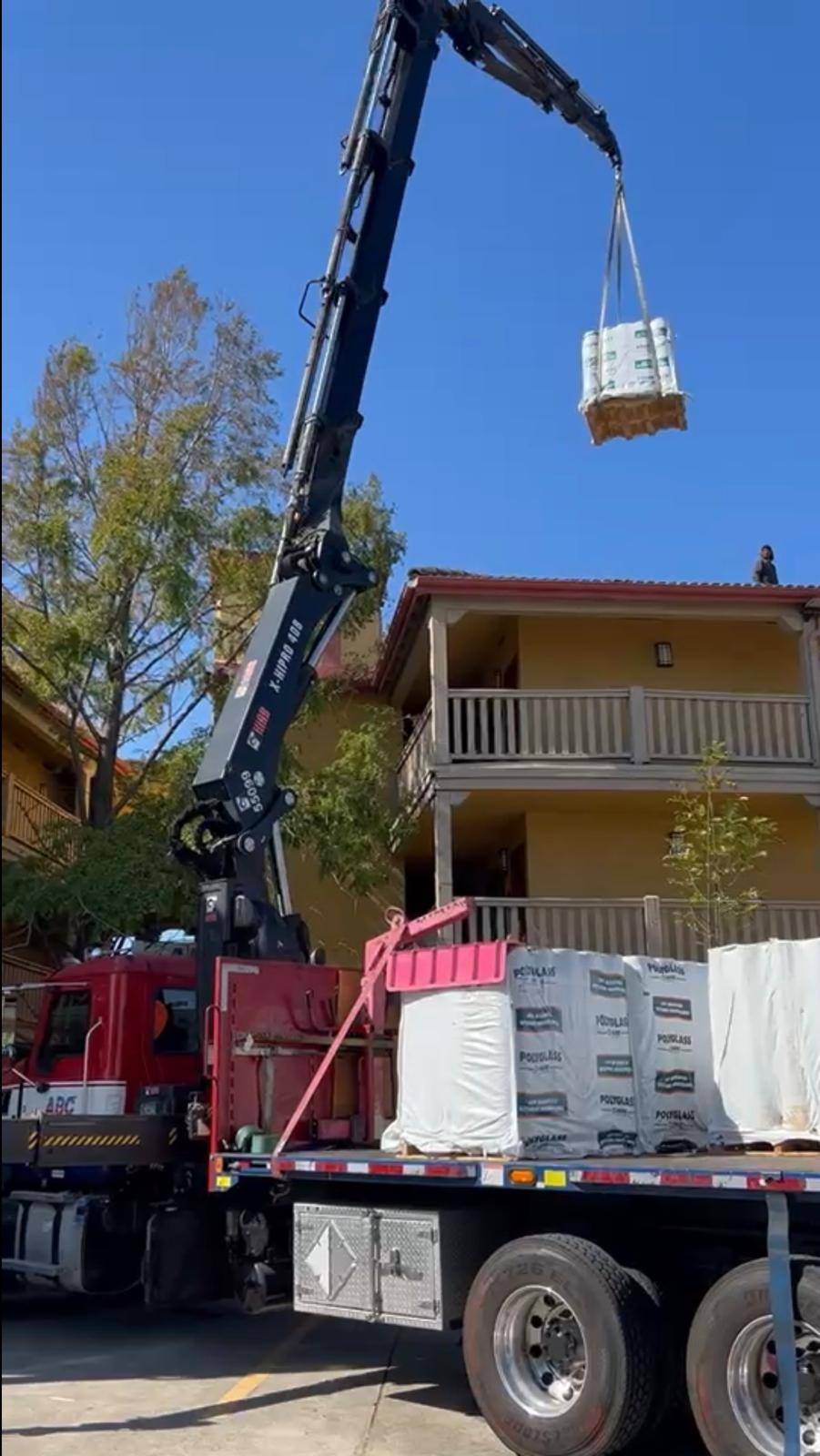 Crane hoisting a bundle of roofing materials onto the tile roof of a multi-story building