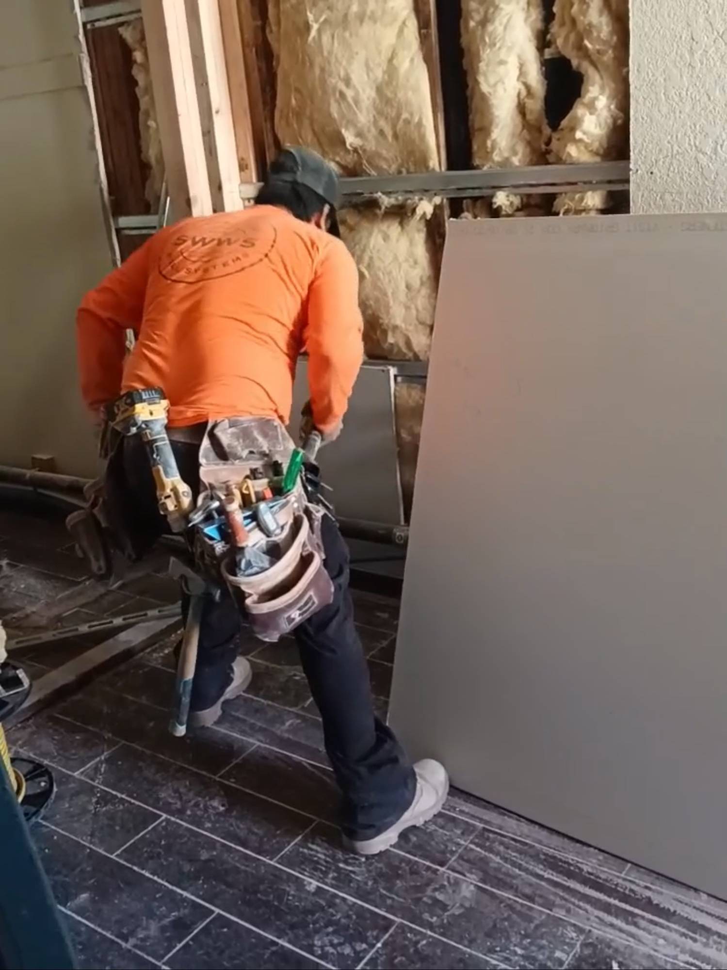 Drywaller positioning a sheet against freshly insulated framing