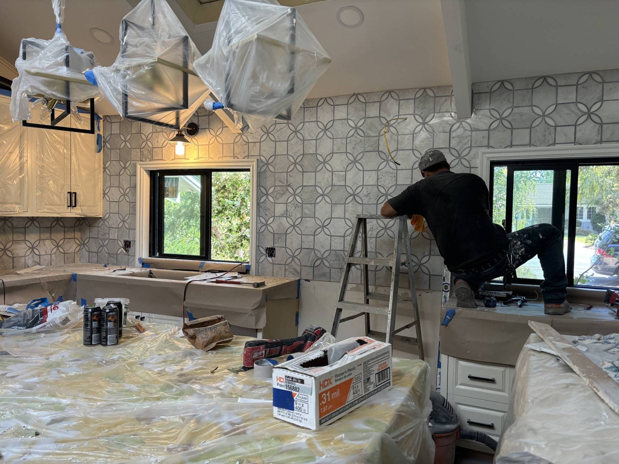 Tile setter finishing a full-height marble mosaic backsplash during a kitchen renovation