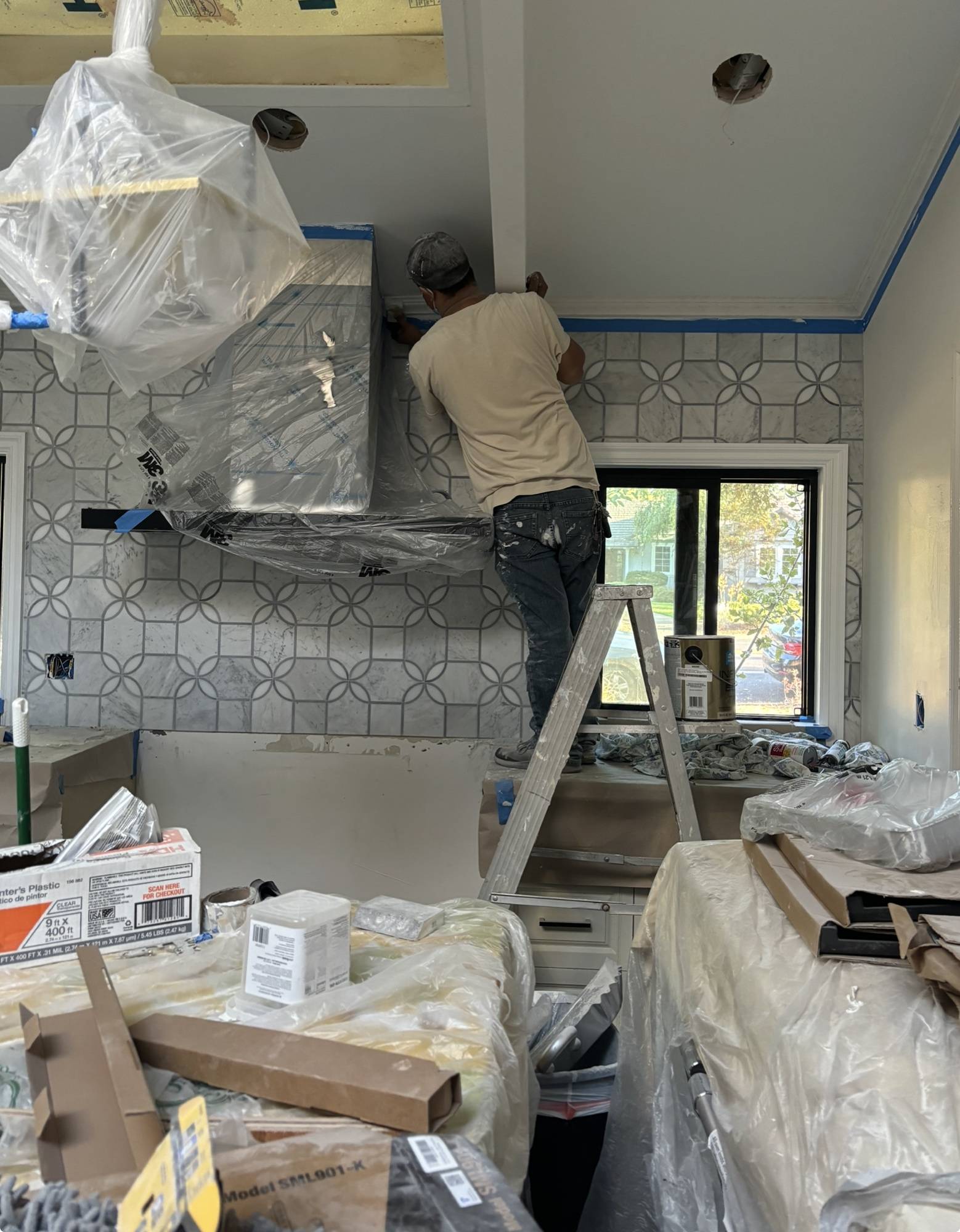 Painter detailing crown molding above a protected range hood during a kitchen renovation